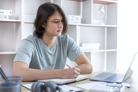 Asian man taking notes in notebook while studying online in laptop at home, V 스톡 사진