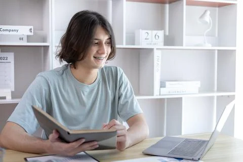 Asian man taking notes in notebook while studying online in laptop at home, V Stock Photos