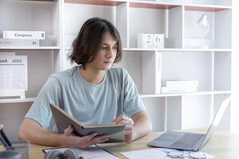 Asian man taking notes in notebook while studying online in laptop at home, V Stock Photos