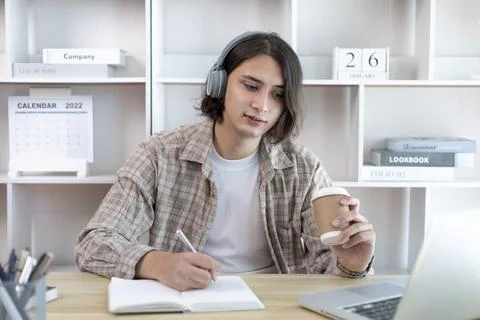 Asian man taking notes in notebook while studying online in laptop at home, V Stock Photos