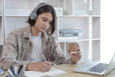 Asian man taking notes in notebook while studying online in laptop at home, V Stock Photos