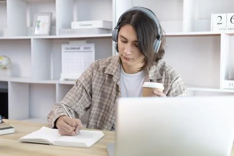 Asian man taking notes in notebook while studying online in laptop at home, V Stock Photos