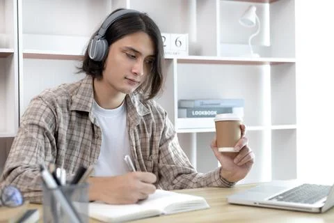Asian man taking notes in notebook while studying online in laptop at home, V Stock Photos
