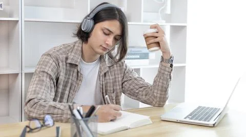 Asian man taking notes in notebook while studying online in laptop at home, V 스톡 사진