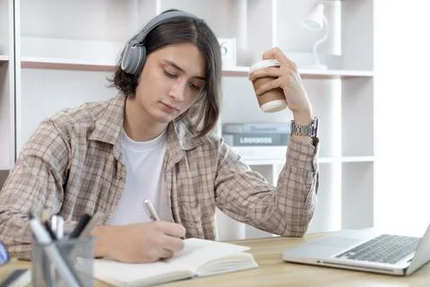 Asian man taking notes in notebook while studying online in laptop at home, V Stock Photos
