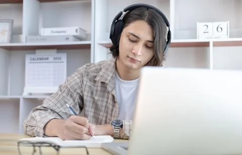 Asian man taking notes in notebook while studying online in laptop at home, V Stock Photos