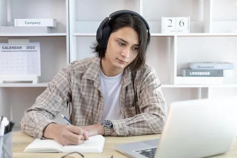 Asian man taking notes in notebook while studying online in laptop at home, V Stock Photos