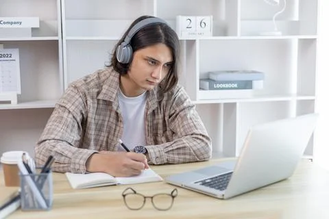 Asian man taking notes in notebook while studying online in laptop at home, V Stock Photos