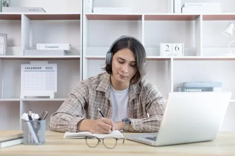Asian man taking notes in notebook while studying online in laptop at home, V Stock Photos