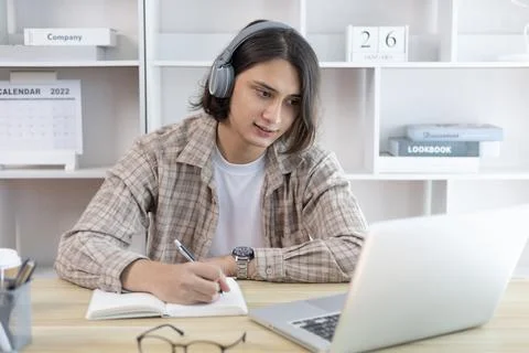 Asian man taking notes in notebook while studying online in laptop at home, V 스톡 사진