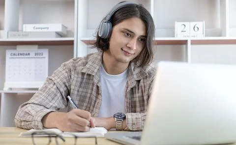Asian man taking notes in notebook while studying online in laptop at home, V 스톡 사진