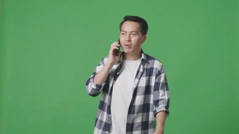 Asian Man Talking On Mobile Phone While Walking On Green Screen In The Studio Stock Footage 248006053
