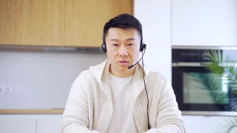Asian man talking online on video call at home room with headset. Male in casual Stock Footage 155315013