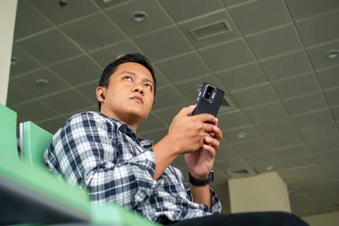 Asian man thingking while using mobile phone in airport waiting area. Male .. Stock Photos
