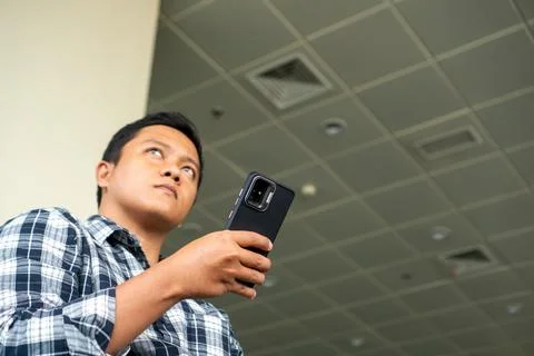 Asian man thingking while using mobile phone in airport waiting area. Male .. Stock Photos