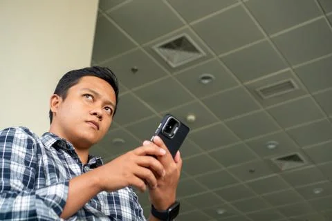 Asian man thingking while using mobile phone in airport waiting area. Male .. Stock Photos