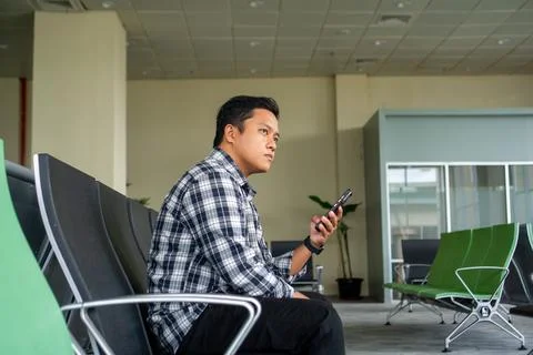 Asian man thingking while using mobile phone in airport waiting area. Male .. Stock Photos