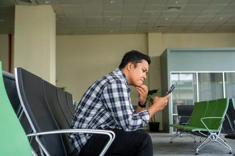 Asian man thingking while using mobile phone in airport waiting area. Male .. Stock Photos