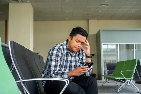 Asian man thingking while using mobile phone in airport waiting area. Male .. Stock Photos