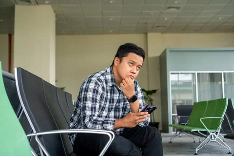 Asian man thingking while using mobile phone in airport waiting area. Male .. Stock Photos
