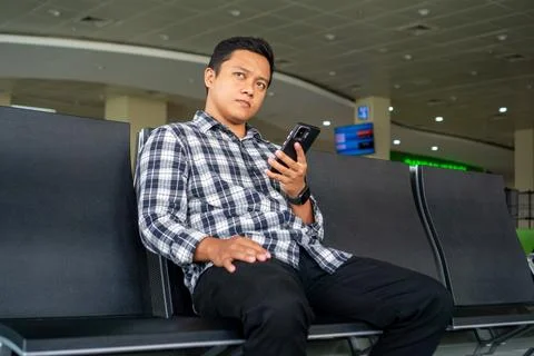 Asian man thingking while using mobile phone in airport waiting area. Male .. Stock Photos