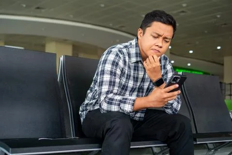 Asian man thingking while using mobile phone in airport waiting area. Male .. Stock Photos