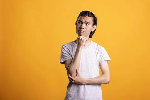 Asian man thinking deeply and touching chin against yellow background Stock Photos