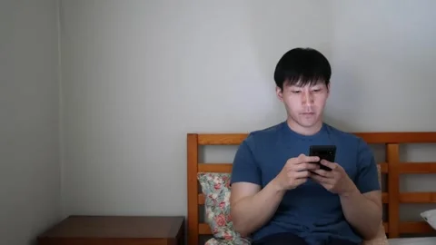 Asian man throws phone on bed  after looking at social media Stock Footage 248652251