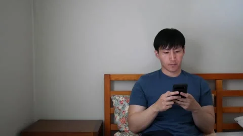 Asian man throws phone on bed  after reading the news Stock Footage 248665474