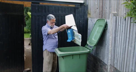 Asian man tipping contents of kitchen waste bin into green bin for recycling Stock Footage