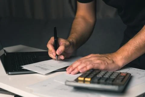 Asian man is using a calculator to calculate expenses while his hand record.. Stock Photos