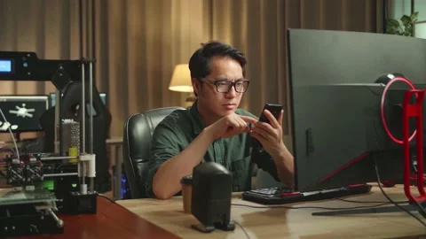 Asian Man Using Mobile Phone While Works On Personal Computer And 3D Printer Stock Footage 158107684