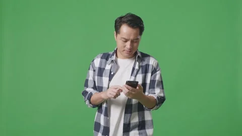 Asian Man Using Mobile Phone While Walking On Green Screen In The Studio Stock Footage 248005996