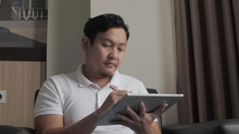 Asian man using pen stylus to draw on his digital tablet while sitting  Stock Footage 160639149