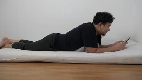 Asian man using phone on bed, reading chat message while lying on matress i.. Video stock 295999769