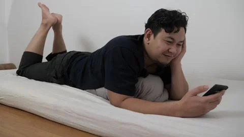 Asian man using phone on bed, reading chat message while lying on matress i.. Video stock 295999785