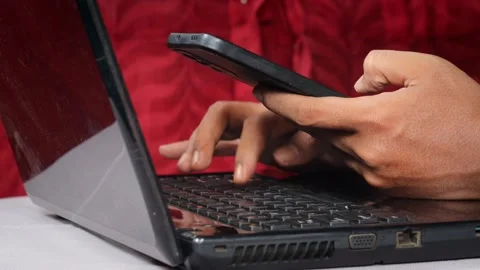 Asian Man using a smartphone while working on a laptop at a desk. Stock Footage 348653221