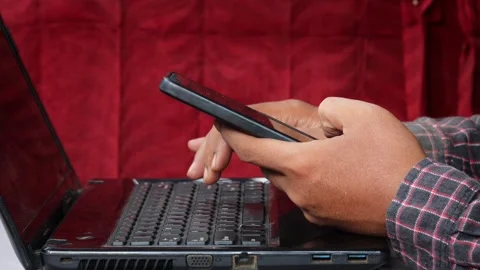 Asian Man using a smartphone while working on a laptop at a desk. Stock Footage 348653224