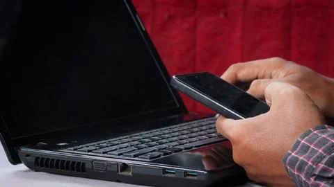 Asian Man using a smartphone while working on a laptop at a desk. Stock Footage 348653231