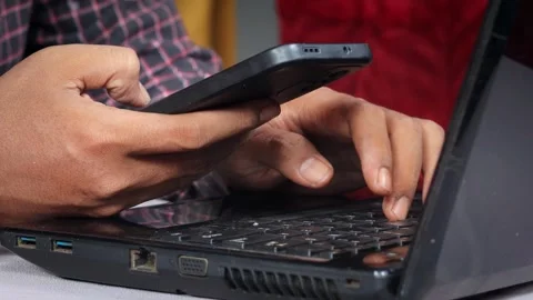 Asian Man using a smartphone while working on a laptop at a desk. Stock Footage 348653233