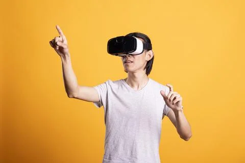 Asian man using VR headset and raising arms in 3D gaming simulation Stock Photos