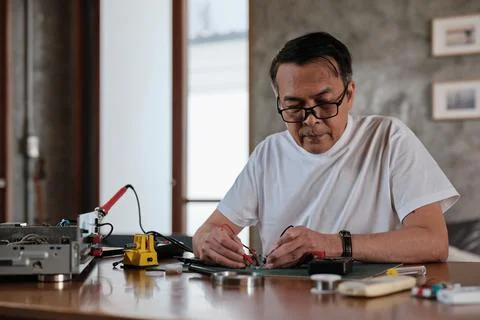 Asian man voltage test on electronics component circuit board with multimeter. Foto stock