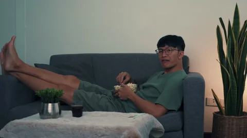 Asian man is watching the series on the sofa in the living room while eating  Stock Footage 150843625