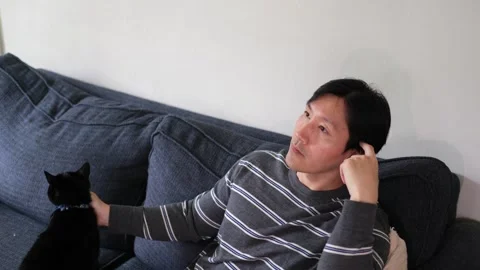 Asian Man watching tv while petting his cat Stock Footage 318189599