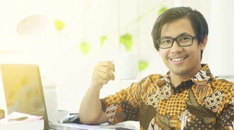 Asian Man Wearing Batik Drinks Coffee and Smiles to The Camera - 4K Resolutio Stock Footage 60615728