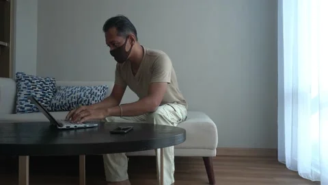 Asian man wearing mask while working from home. using laptop in the living room Stock Footage 226948045