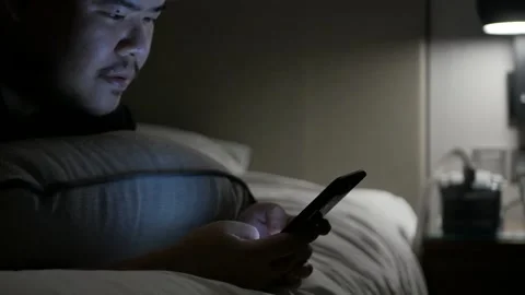 Asian man while chatting on mobile phone and lay on the bed in bed room in ni Video stock 271616370