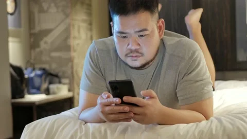 Asian man while using chatting on mobile phone and lay on the bed in bed room Stock Footage 166229264