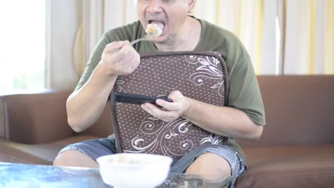 Asian man who is using his mobile device while eating food. 스톡 동영상 250370002