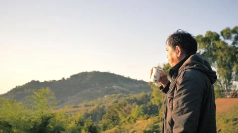 Asian man in a winter jacket enjoys a hot drink while Stock Footage 324906484